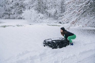 Frau versucht, einen großen Reifen im Schnee anzuheben - ISF04006