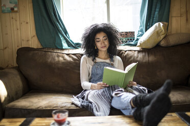Young woman sitting on sofa, reading book - ISF04011