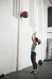 Frau wirft Fitness-Ball gegen die Wand im Cross-Training-Fitnessstudio - ISF04053