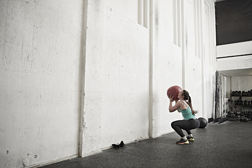 Frau wirft Fitness-Ball gegen die Wand im Cross-Training-Fitnessstudio - ISF04054