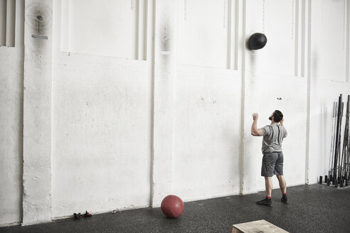 Mann wirft Fitness-Ball gegen die Wand im Cross-Training-Fitnessstudio - ISF04056