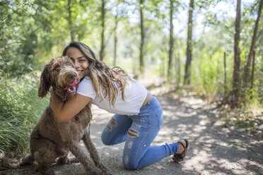 Porträt eines Teenager-Mädchens, das einen süßen Hund auf einem Waldweg umarmt - ISF04157