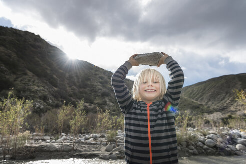 Porträt eines niedlichen Jungen, der einen Stein aus dem Flussbett hochhält - ISF04201