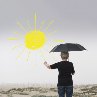 Ältere Frau mit Regenschirm zeichnet Sonne in die Luft - ISF04211