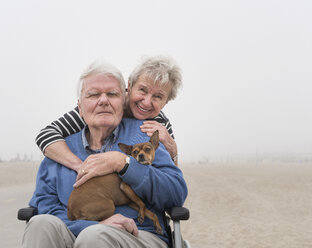 Porträt eines älteren Mannes im Rollstuhl mit Frau und Hund am Strand, Santa Monica, Kalifornien, USA - ISF04240
