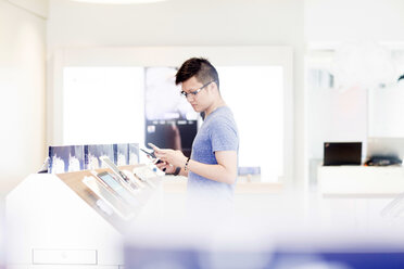 Man shopping in technology shop looking at smartphone - ISF04276