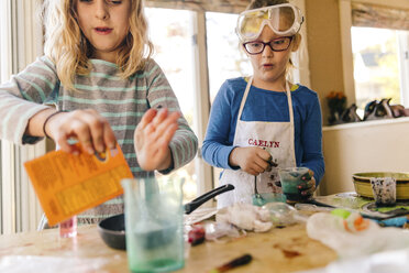 Two girls doing science experiment, pouring packet into frying pan - ISF04297