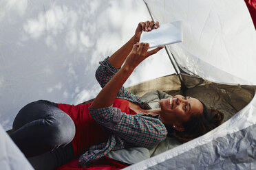 Mittlere erwachsene Frau beim Zelten, liegend im Zelt, die ein digitales Tablet-Selfie macht - ISF04303