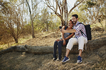 Active midlife couple captures memories on their hike, pausing to snap a selfie on a rustic log - ISF04304