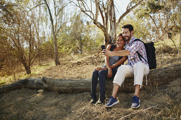 Ein aktives Paar im mittleren Alter hält auf seiner Wanderung Erinnerungen fest und macht ein Selfie auf einem rustikalen Baumstamm - ISF04304