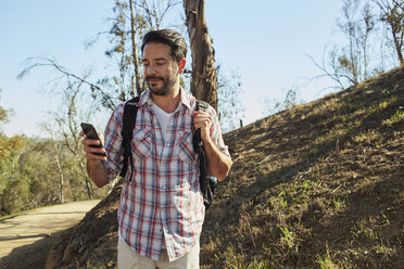 Mid adult man hiking, looking at smartphone - ISF04307