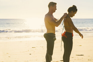 Mann hilft Freundin beim Anziehen des Neoprenanzugs am Newport Beach, Kalifornien, USA - ISF04313