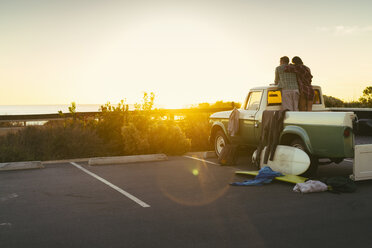 Rückansicht eines Paares auf dem Rücksitz eines Pickups, das den Sonnenuntergang in Newport Beach, Kalifornien, USA, beobachtet - ISF04329