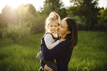 Portrait of woman kissing her daughter in sunlit field - ISF04391