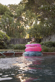 Young girl, standing in the middle of inflatable rings in outdoor swimming pool - ISF04404