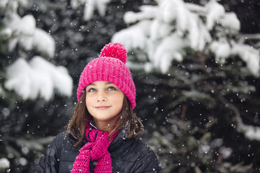 Girl in pink knitted hat looking up at falling snow - ISF04424