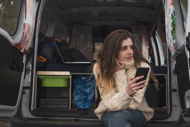 Porträt einer jungen Frau mit Handy, die in einem Lieferwagen sitzt - KKAF01022