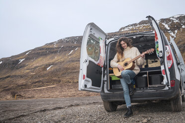 Iceland, woman in front of van playing guitar - KKAF01024