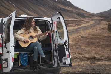 Iceland, woman in front of van playing guitar - KKAF01025