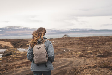 Island, Rückenansicht einer Frau mit Rucksack beim Wandern in der Landschaft - KKAF01028