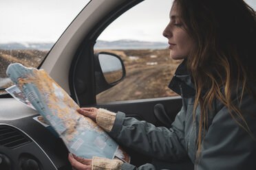 Iceland, young woman in car looking at map - KKAF01030