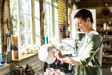 Woman pouring liquid into preserves jars in kitchen - ISF04510