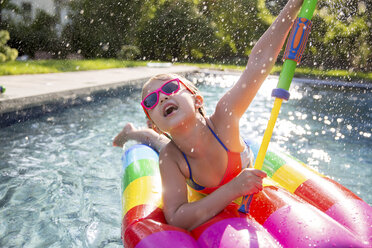 Mädchen im Bikini auf Hüpfburg spielt mit Wasserpistole im Freibad - ISF04523