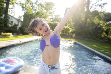 Boy in seashell bikini top dancing by outdoor swimming pool - ISF04525