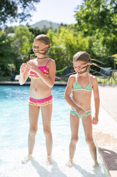Two sisters shaking wet hair by outdoor swimming pool - ISF04528