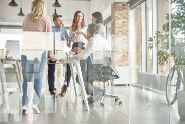 View through glass of colleagues standing in office talking - ISF04569