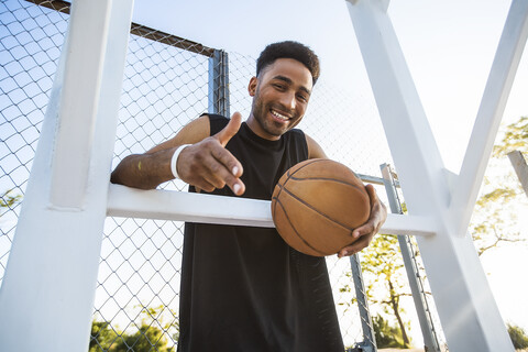 Porträt eines jungen Mannes, der einen Basketball in der Hand hält, lächelnd, Flachwinkelansicht, lizenzfreies Stockfoto