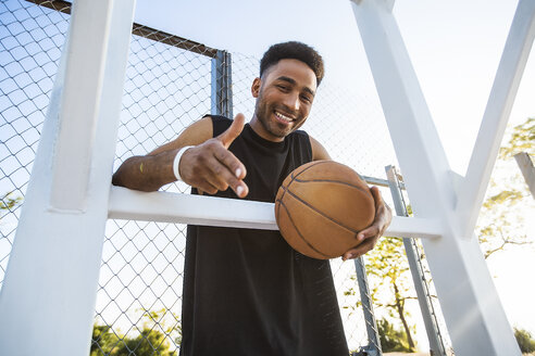 Porträt eines jungen Mannes, der einen Basketball in der Hand hält, lächelnd, Flachwinkelansicht - ISF04572