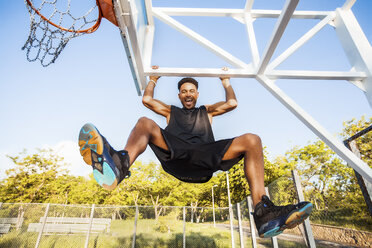 Young man on basketball court, swinging on basketball net frame, low angle view - ISF04573