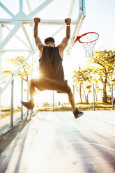 Junger Mann auf Basketballplatz, schwingt auf Basketballkorbrahmen, Rückansicht - ISF04576