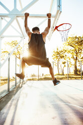 Young man on basketball court, swinging on basketball net frame, rear view - ISF04576