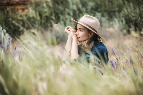 Mittlere erwachsene Frau im langen Gras sitzend, nachdenklicher Gesichtsausdruck, lizenzfreies Stockfoto