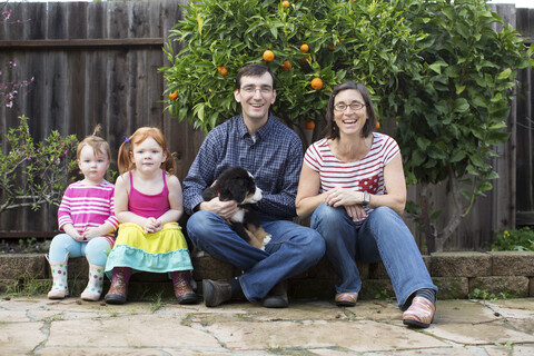 Porträt einer jungen Familie mit Hund, sitzend im Garten, lizenzfreies Stockfoto