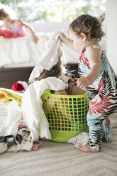 Female toddler removing laundry from child hiding in laundry basket - ISF04645