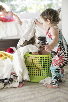 Weibliches Kleinkind entfernt Wäsche von einem Kind, das sich im Wäschekorb versteckt - ISF04645