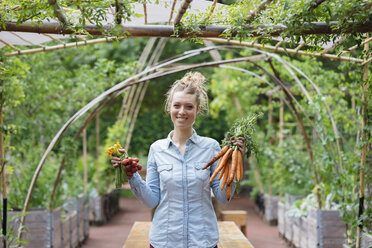 Woman in garden holding bunches of carrots smiling - ISF04671