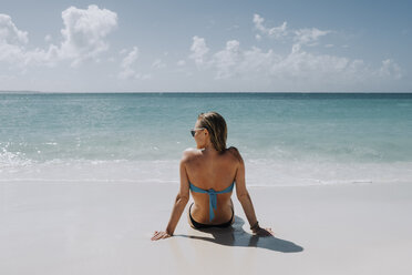 Rückansicht einer Frau im Bikini, die am Strand sitzt und auf das blaue Meer hinausschaut, Anguilla, Saint Martin, Karibik - ISF04726