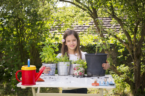 Portrait of proud little girl with potted spice plants on table in the garden stock photo