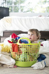 Female toddler sitting in basket amongst laundry - ISF04755