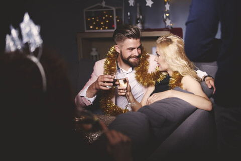 Mann und Frau auf einer Party, auf dem Sofa sitzend, mit Getränken in der Hand, die einen Toast aussprechen, lizenzfreies Stockfoto