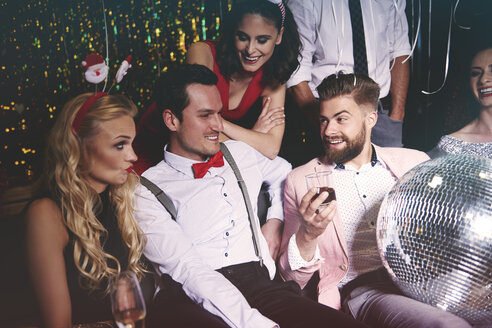 Eine Gruppe von Freunden sitzt auf einer Party zusammen, ein Mann hält eine Discokugel im Schoß - ISF04766