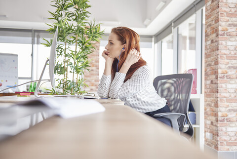 Frau sitzt am Schreibtisch und schaut weg, lizenzfreies Stockfoto