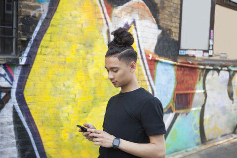 Junger Mann, der im Freien spazieren geht und sein Smartphone benutzt, lizenzfreies Stockfoto