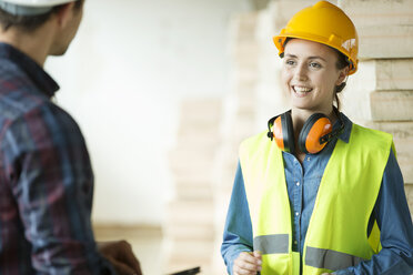 Two people standing in constructions site, wearing hard hats, having discussion - ISF04846