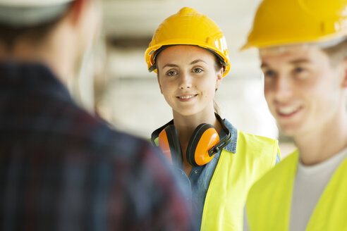 Three people standing in constructions site, wearing hard hats, having discussion - ISF04847