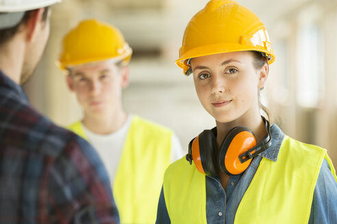 Portrait of woman wearing hard hat and hi vis vest, co-workers in background - ISF04849